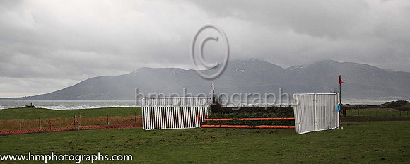 A rain shower hovers over the Mourne Mountains with a fence a the East Down P2p at Tyrella in the foreground
