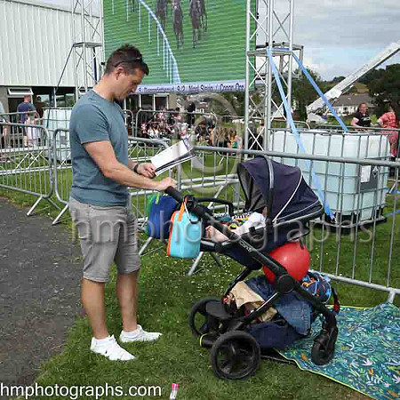 Spectator checking form whilst carrying out domestic duties at The Family Fun Raceday at Downpatrick Race Course on Wednesday 13th July 2022.